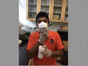 Rashad in a mask holding a white container in the lab